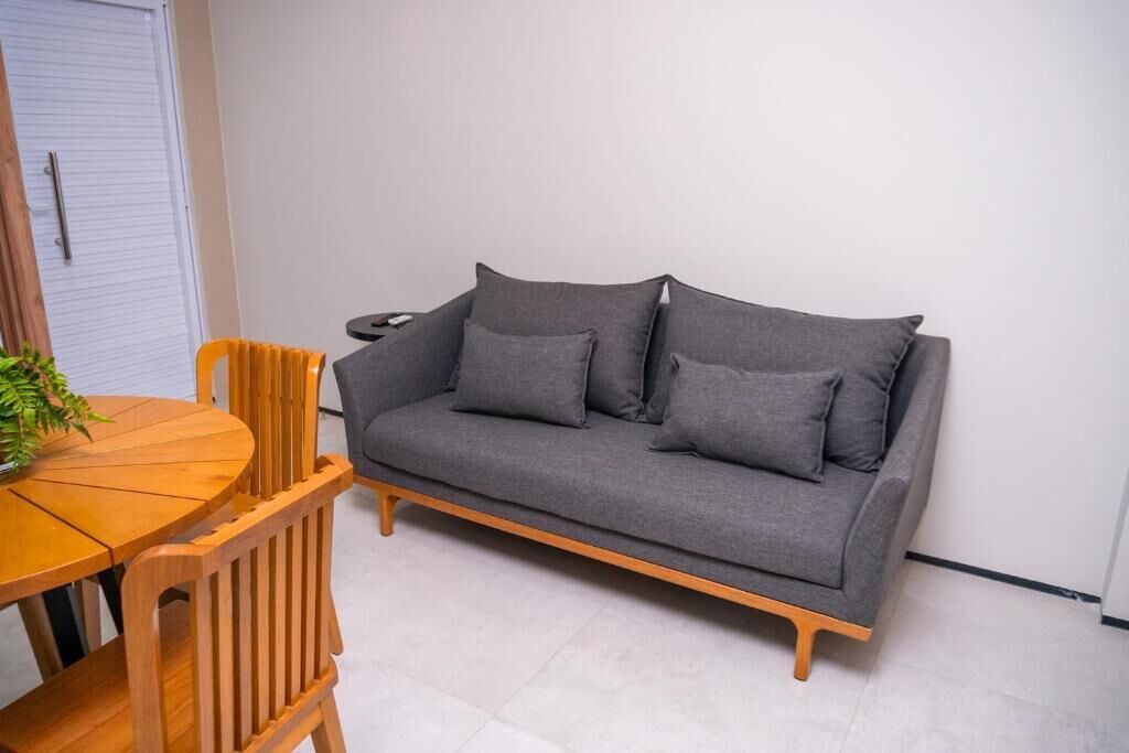 Un sofá gris con patas de madera, una mesa de comedor de madera y dos sillas de madera.
