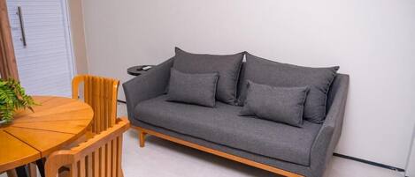 Un sofá gris con patas de madera, una mesa de comedor de madera y dos sillas de madera.