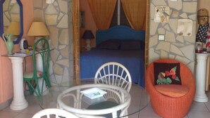 Una habitación con una cama, una mesa redonda de vidrio, dos sillas, una lámpara y un adorno en la pared.