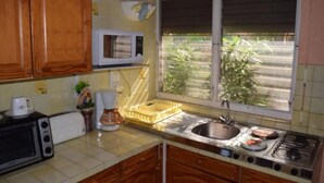 Una cocina con armarios de madera, microondas, fregadero, estufa y ventana con vistas a la vegetación.