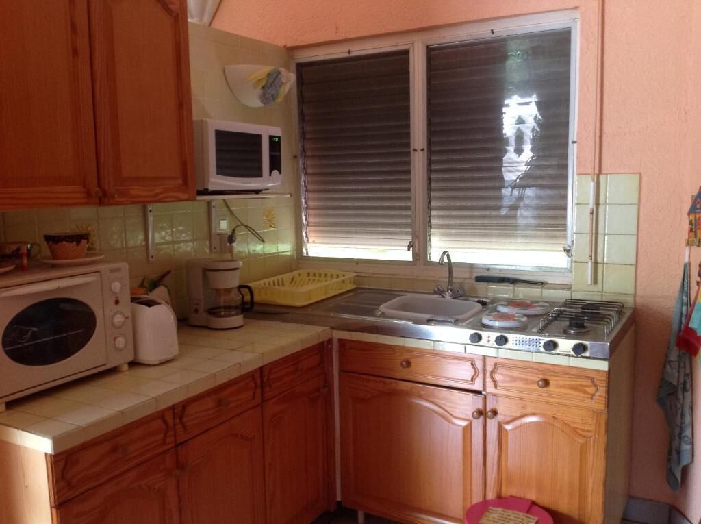 A compact kitchen with wooden cabinets, a microwave, a coffee maker, a sink, and a window with blinds.