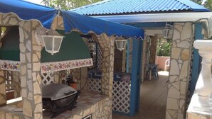 Un espacio exterior cubierto con paredes de piedra, una parrilla y una silla blanca.