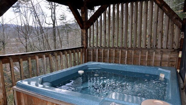 A hot tub in a wooden cabin with a view of trees and mountains.