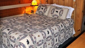 A bed with a patterned quilt, a bedside lamp, and wooden paneling on the walls.