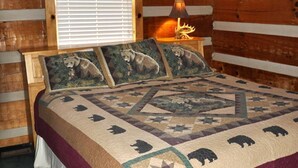 Camera da letto in una baita di legno con un letto con copripiumino a fantasia animalier, un comodino con una lampada e una finestra con persiane.