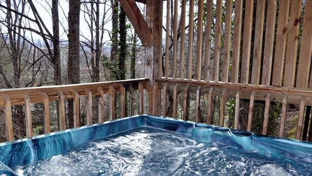 Una vasca idromassaggio in un'area con decking in legno, circondata da alberi.