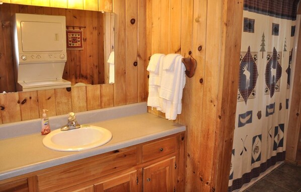 A wooden cabin bathroom with a sink, mirror, towel rack, and a wall-mounted heater.