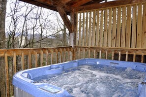 A hot tub with a wooden deck and a view of trees.