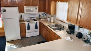 Eine kompakte Küche mit Holzausstattung, inklusive Kühlschrank, Mikrowelle, Herd, Spüle und Kaffeemaschine.