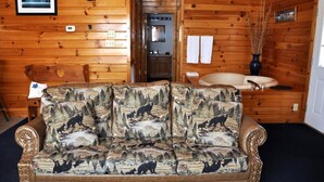 Ein Blockhaushaus-Interieur mit einer Couch mit Bärenmuster, einer Holz-Wand-Uhr und einem Badezimmer mit einer Badewanne.