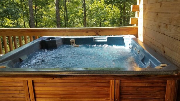 Un jacuzzi con una terraza de madera y vistas a árboles.