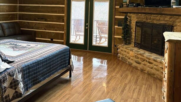 Ein Blockhauszimmer mit Bett, Kamin und einer Tür zu einer Terrasses.