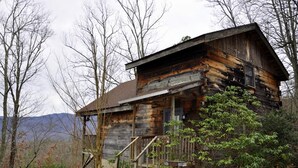 Eine rustikale Holzhütte mit Veranda und Treppe, umgeben von Bäumen und Bergen.