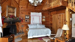 Ein gemütliches Schlafzimmer in einer Blockhütte mit Kamin, einem Bett, einem Fernseher und einer Chandelüster.