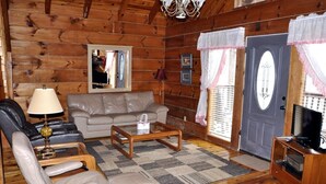 Ein gemütliches Blockhaus-Interieur mit einer Couch, Sesseln, einem Couchtisch und einem Fernseher.