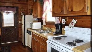 A rustic kitchen with wooden cabinets, a white stove, a microwave, and a coffee maker. - Romantic Secluded Cabin in Gatlinburg with Great Mountain View (Gatlinburg)
