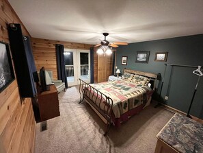 A bedroom with a bed, a ceiling fan, a window with curtains, and a door leading to a balcony.