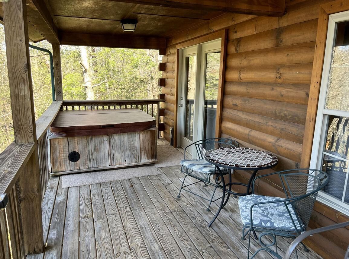 A wooden deck with a hot tub, a round table with chairs, and a glass door leading to a covered area.