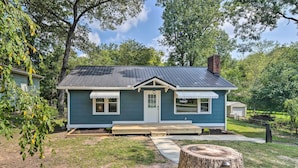 A single-story house with a front porch, a small deck, and a tree stump with a plaque. - Cozy Arden Cottage, 2 Mi to Lake Julian Park! (Arden)