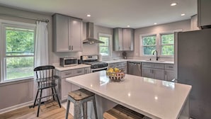 A modern kitchen with grey cabinets, a central island, and a view of greenery outside. - Cozy Arden Cottage, 2 Mi to Lake Julian Park! (Arden)