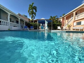 Une piscine d’un bleu éclatant, avec des chaises longues et une statue en arrière-plan.