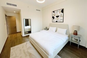 A hotel room with a large bed, a bedside table with a lamp, a mirror, and a wall-mounted artwork. - Enchanting 1BDR Apt w/ Direct Pool & Gym Access (Arjan)