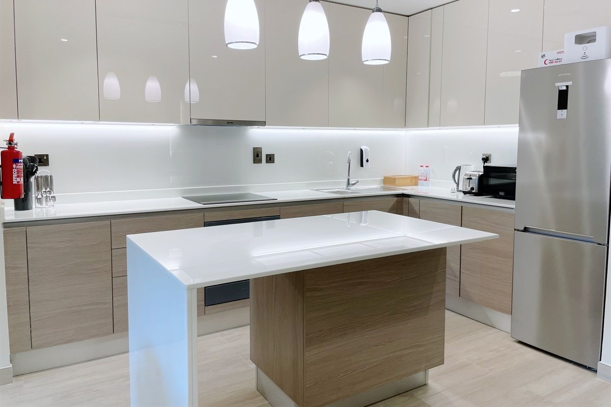 Une cuisine moderne dotée d’un îlot central, d’appareils électroménagers en acier inoxydable et de luminaires suspendus.