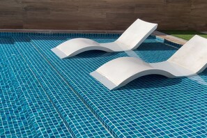 Ein Swimmingpool mit blau gefliestem Boden und zwei weißen Liegestühlen.