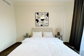 Ein Hotelzimmer mit einem großen Bett, zwei Nachttischen, einem Wandbild und einem Fenster mit Vorhängen.