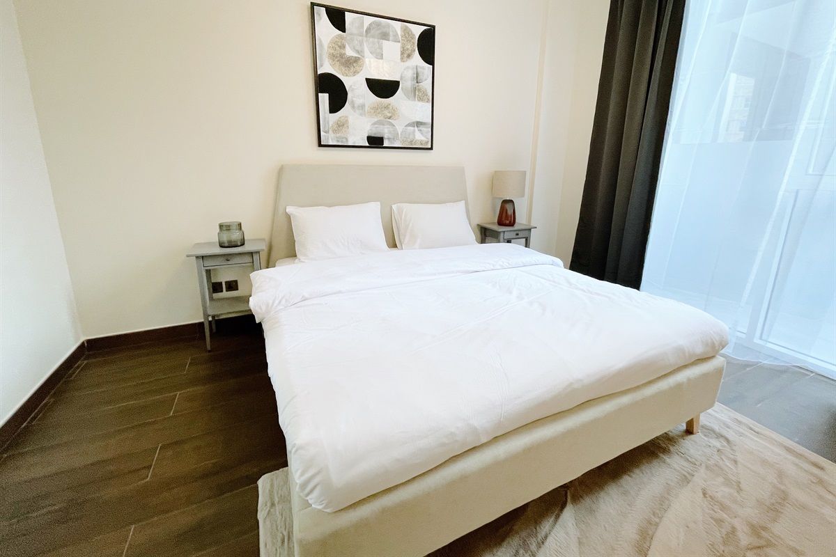 A hotel room with a large bed, a bedside table with a lamp, a wall-mounted artwork, and a window with curtains.