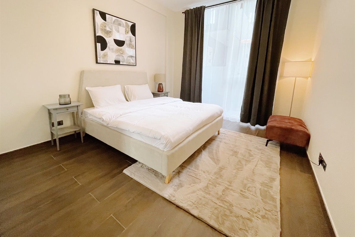 A bedroom with a bed, a nightstand, a lamp, a rug, and a window with curtains.