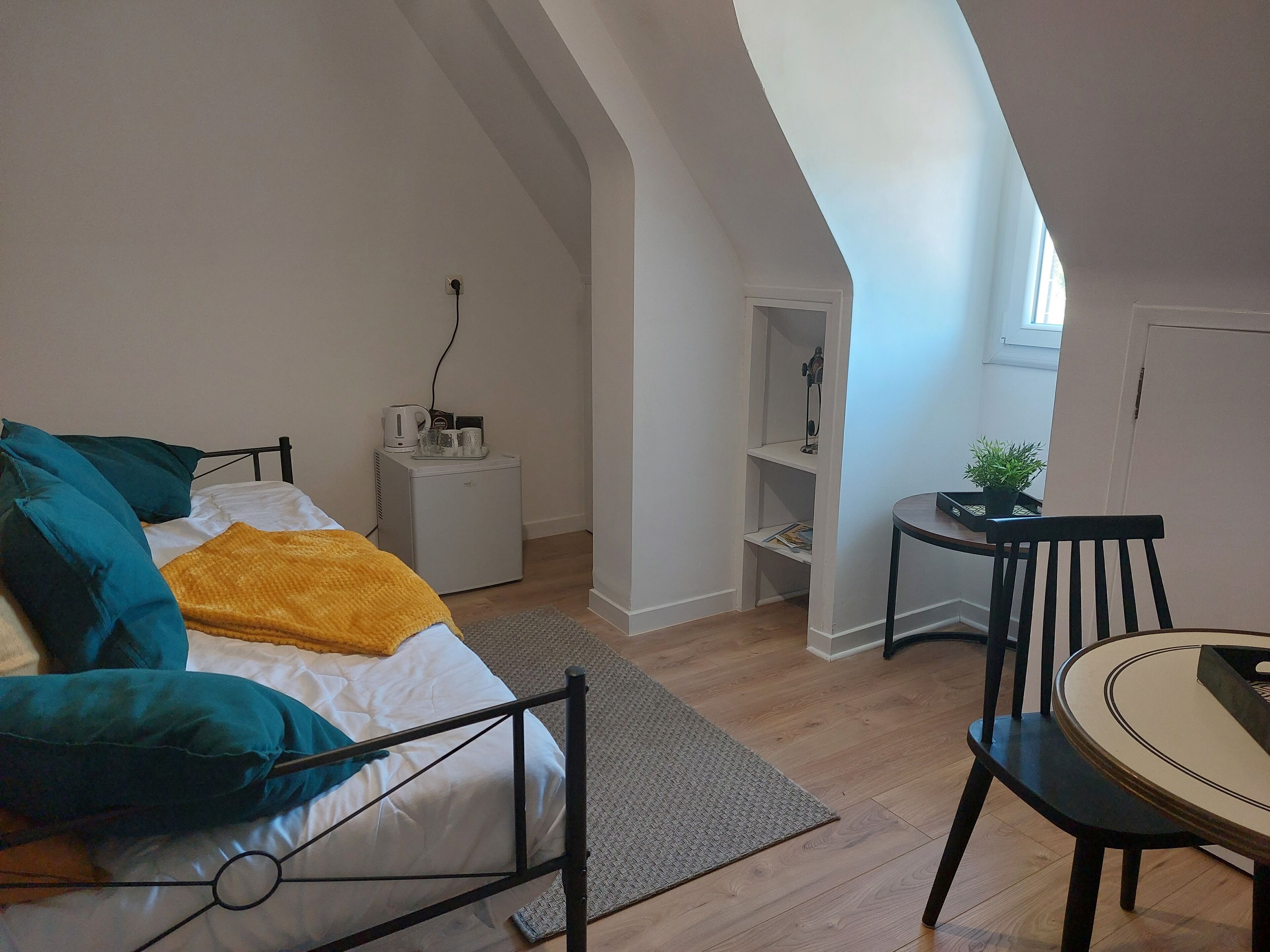 A bedroom with a bed, a nightstand, a small table with a plant, and a chair.