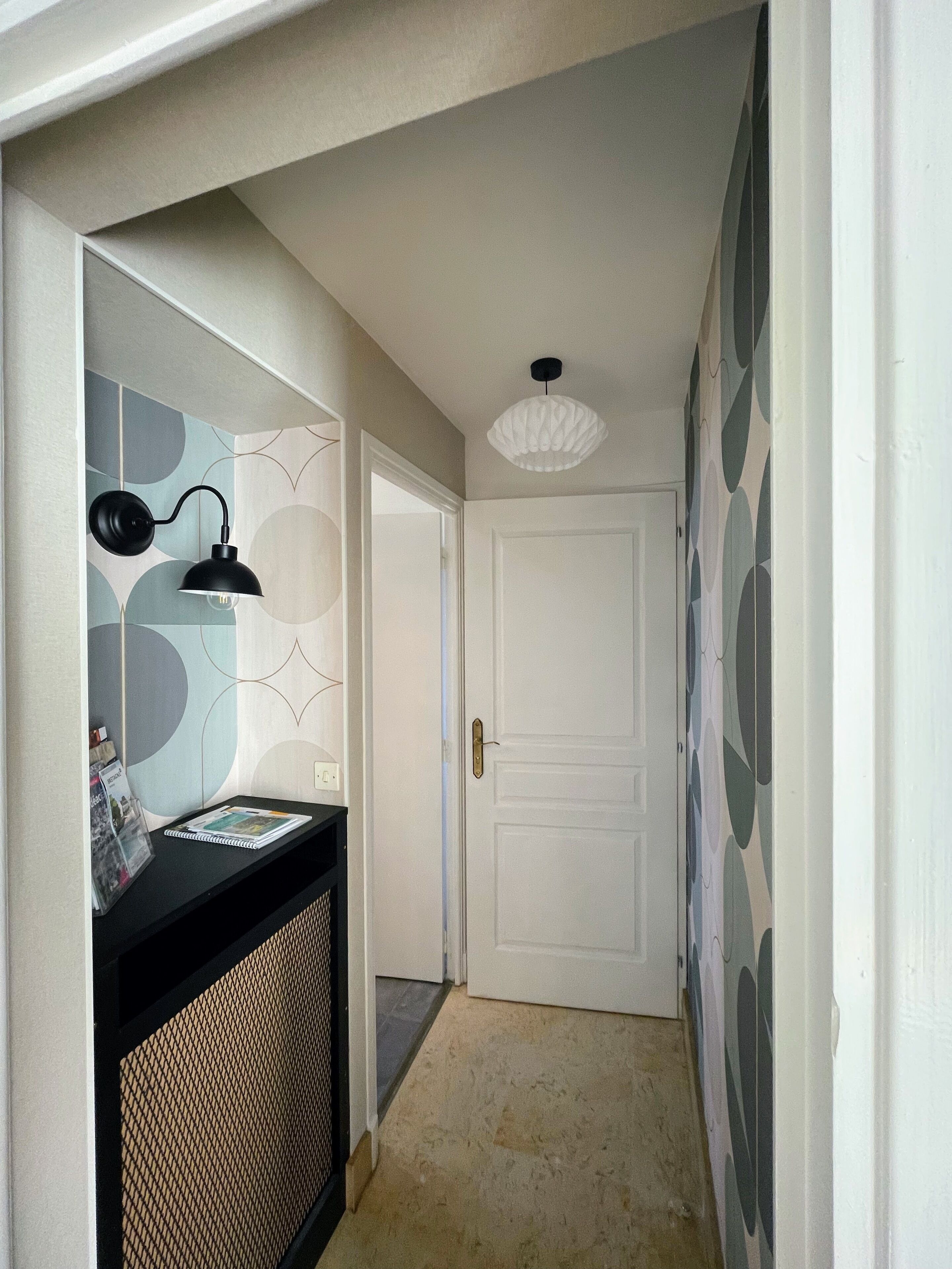 A hallway with a black console table, a white door, and patterned wallpaper.