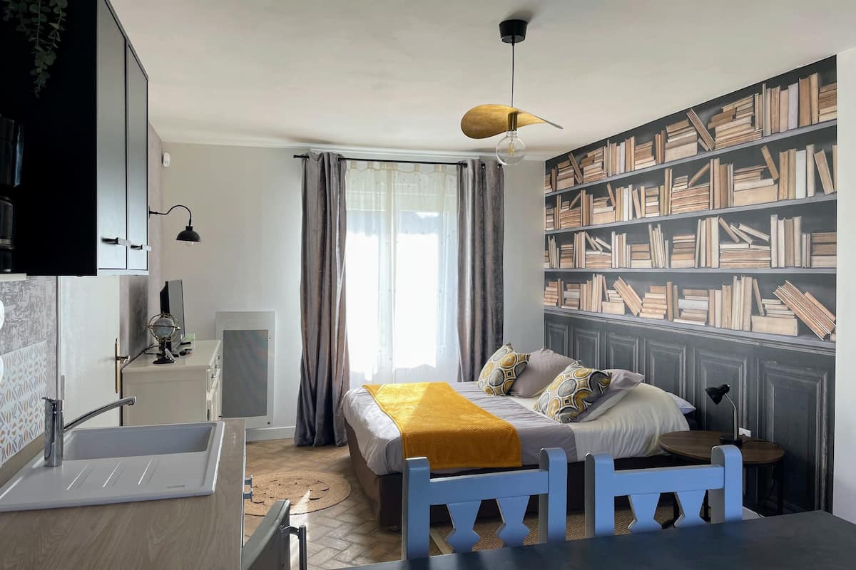 Ein modernes Schlafzimmer mit Bett, Schreibtisch, Bücherregal und einem Fenster mit Vorhängen.
