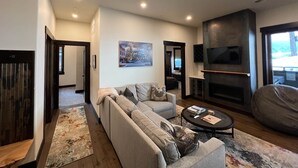 En moderne stue med sofa, sofabord og pejs. Der er et tv ophængt på væggen, og et vindue med udsigt.