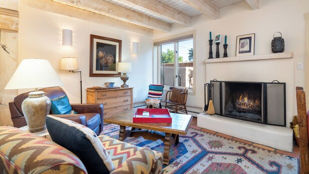 Una sala de estar acogedora con chimenea, vigas de madera, un sofá, una mesa de centro y una alfombra estampada.