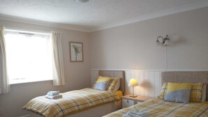 Ein Hotelzimmer mit zwei Betten, jedes mit einer Karo-Bettdecke, einem Nachttisch mit Lampe und einem Fenster mit Vorhängen.