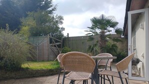 Eine Terrasse im Freien mit Korbstühlen und einem Tisch, umgeben von einem Holzzaun und Grünpflanzen.