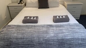 A neatly made bed with a grey and white textured blanket, two pillows, and two folded towels on the bed. - Tumby Bay Motel (Tumby Bay)