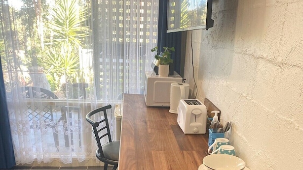 A dining area with a wooden table, two chairs, a microwave, a toaster, and a small potted plant. - Tumby Bay Motel (Tumby Bay)