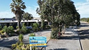 A motel sign with a welcoming message, a palm tree, and a building with solar panels in the background. - Tumby Bay Motel (Tumby Bay)
