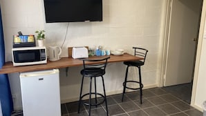 A compact kitchenette with a microwave, toaster, and small refrigerator. There are two black bar stools and a flat-screen TV mounted on the wall. - Tumby Bay Motel (Tumby Bay)