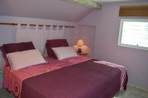 Une chambre à coucher avec un lit, deux oreillers, une lampe de chevet, une fenêtre et un rideau.