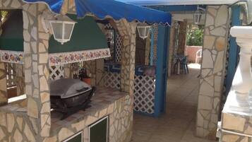 A covered outdoor area with stone walls, a barbecue grill, and a white chair.