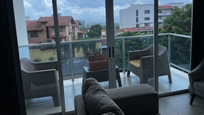 A balcony with a sofa and chairs, a potted plant, and a view of buildings and greenery.