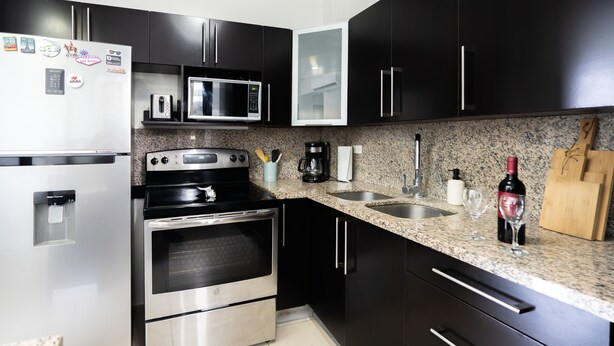 A modern kitchen with stainless steel appliances, a granite countertop, and black cabinetry.