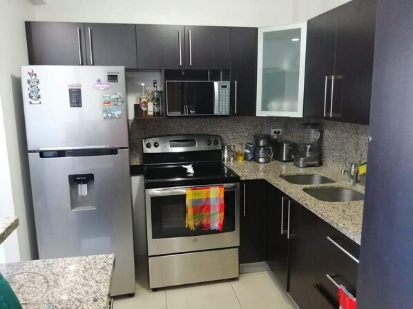 Una cocina moderna con electrodomésticos de acero inoxidable, encimeras de granito y armarios oscuros.
