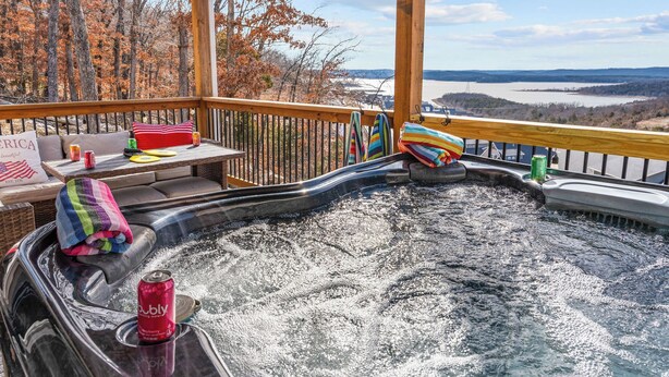 Ein Whirlpool mit Holzterrasse, umgeben von Herbstbäumen und Blick auf einen See.