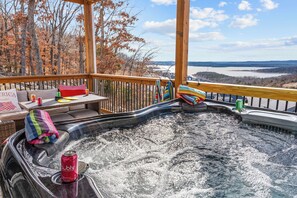 Een hottub met een houten terras, omgeven door herfstbomen en uitzicht op een meer.