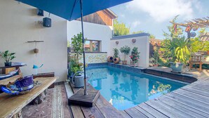 Ein Pool mit Holzterrasse, blauem Sonnenschirm und Topfpflanzen.
